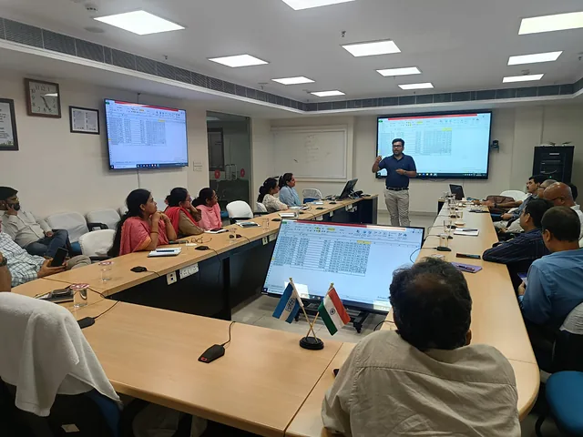 Participants watching a presenter in a boardroom with large screens